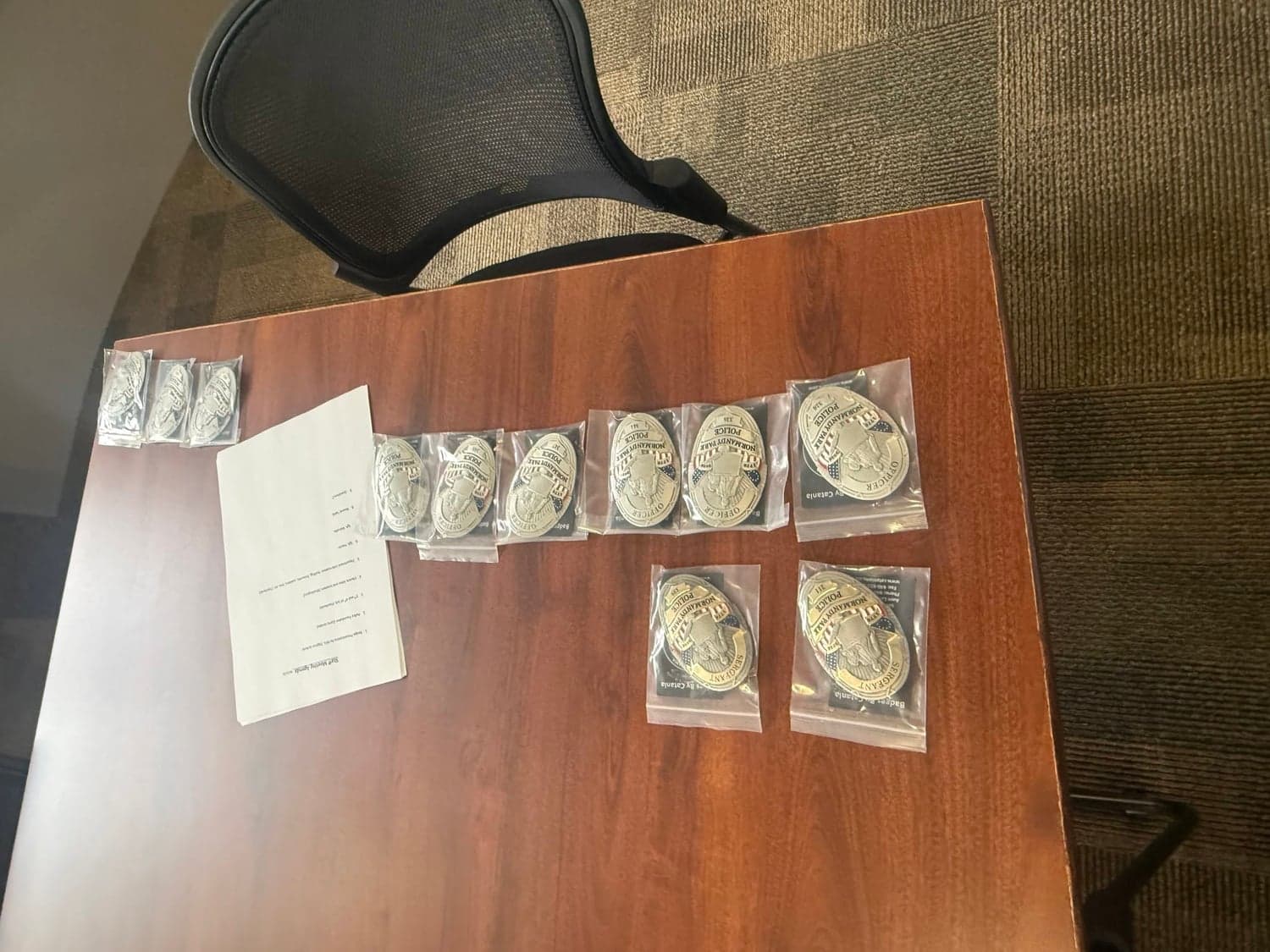 Commemorative police badges in clear sleeves laid out on a wooden table beside a printed sheet.